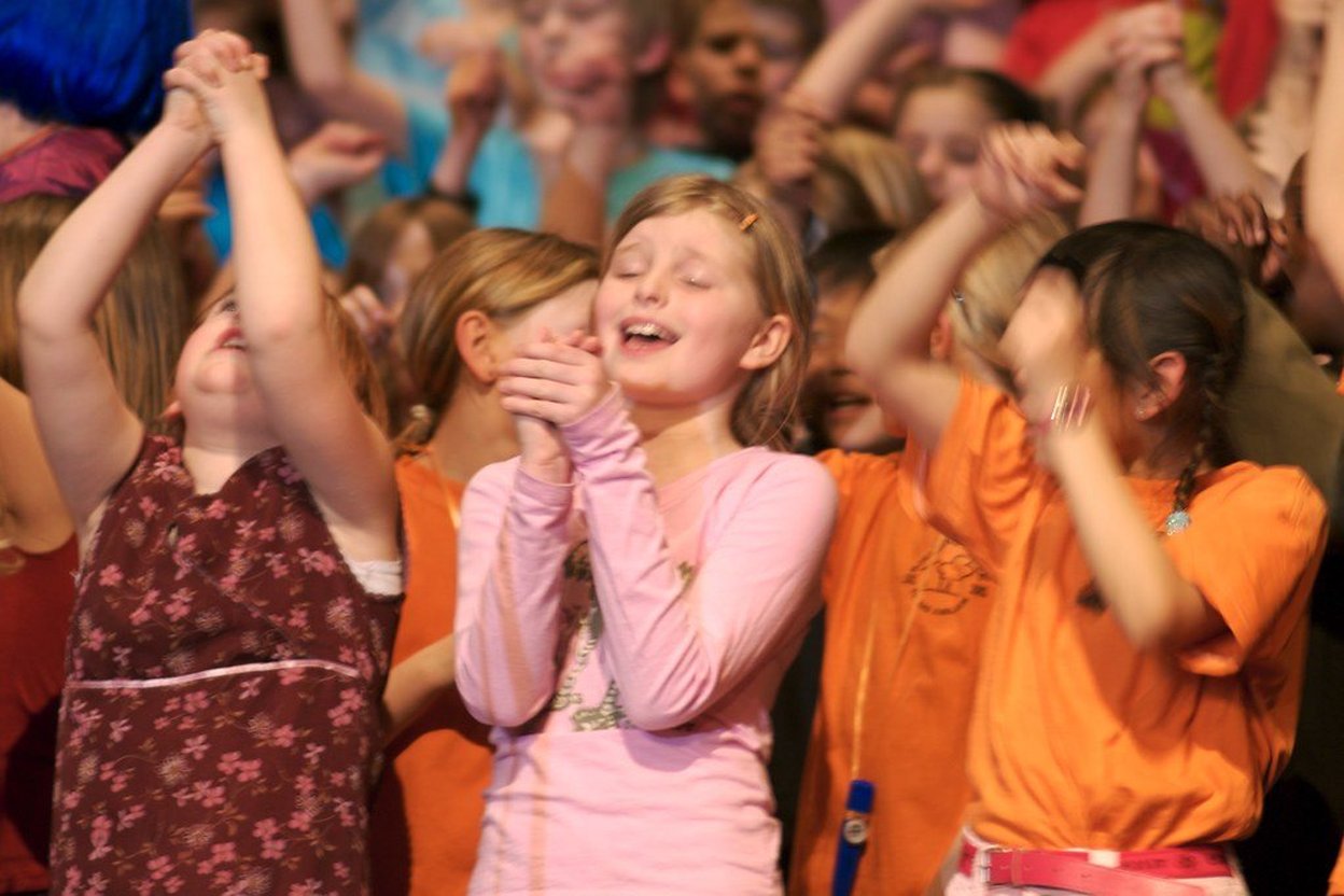 Children raising their hands while they sing together.