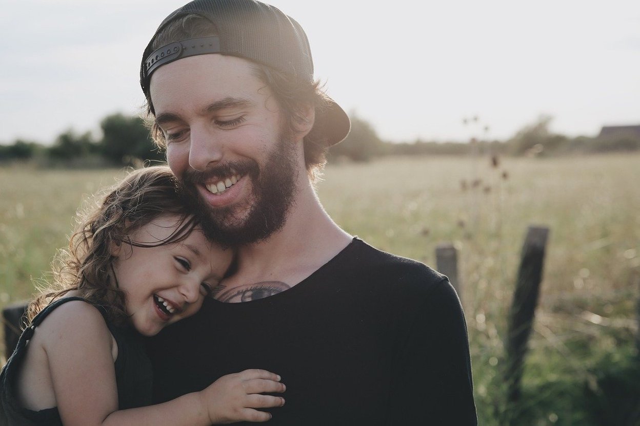 Father and daughter smiling together in a sunny field.