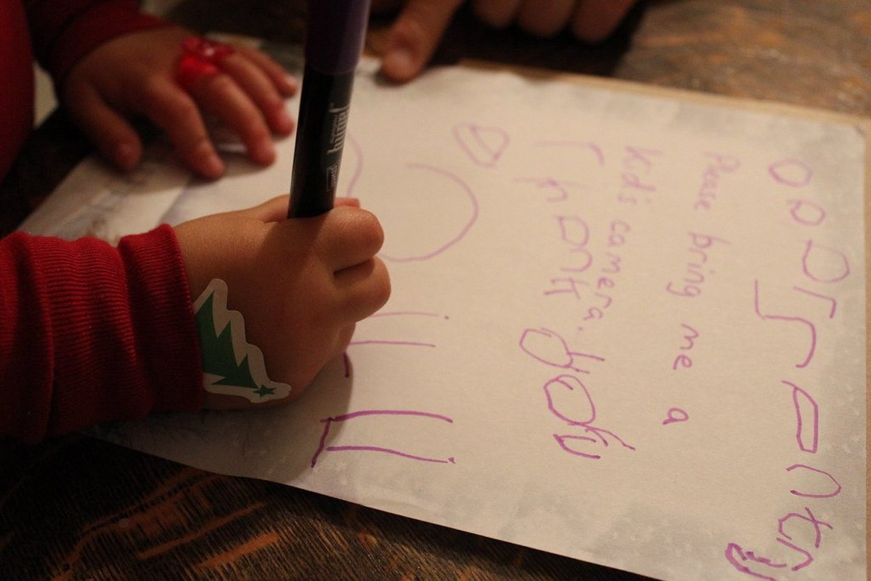 Child writing a note with a purple marker on a piece of paper.