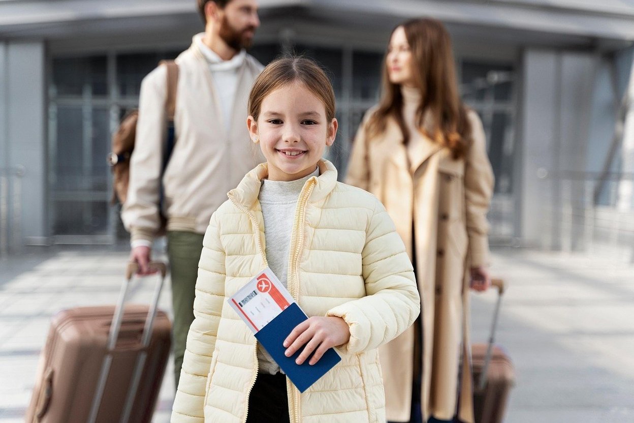 A smiling child holding a passport and boarding pass at the airport.