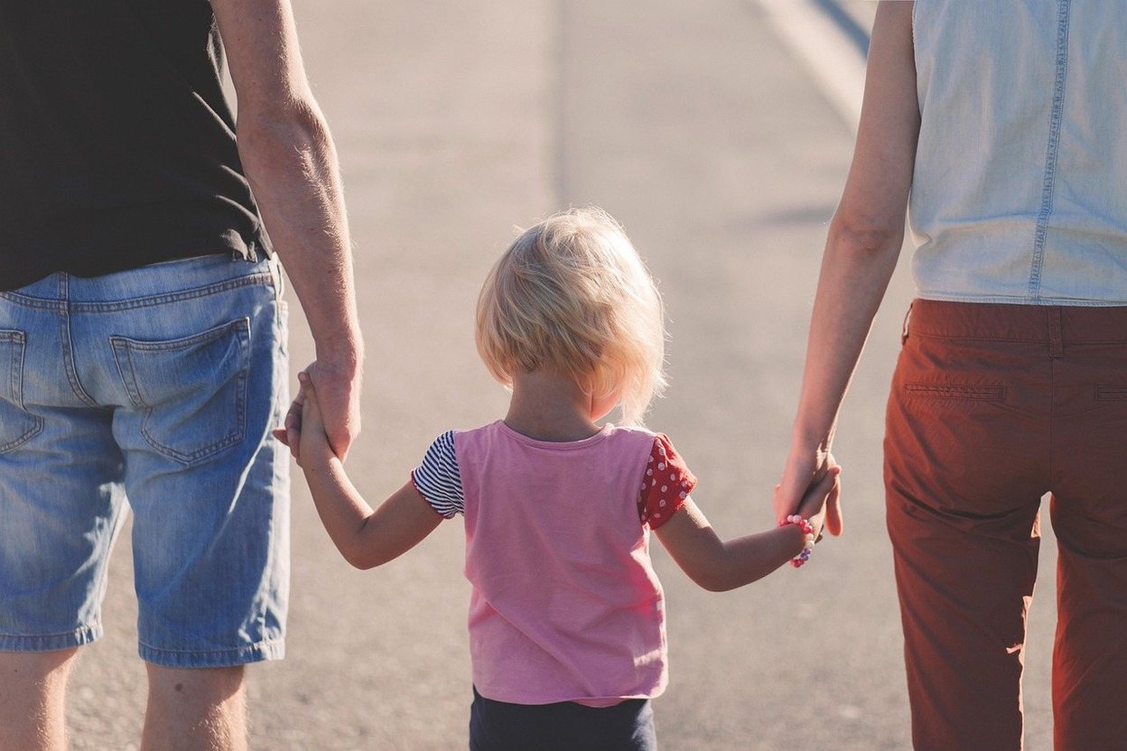 Two adults holding hands with a child walking ahead.