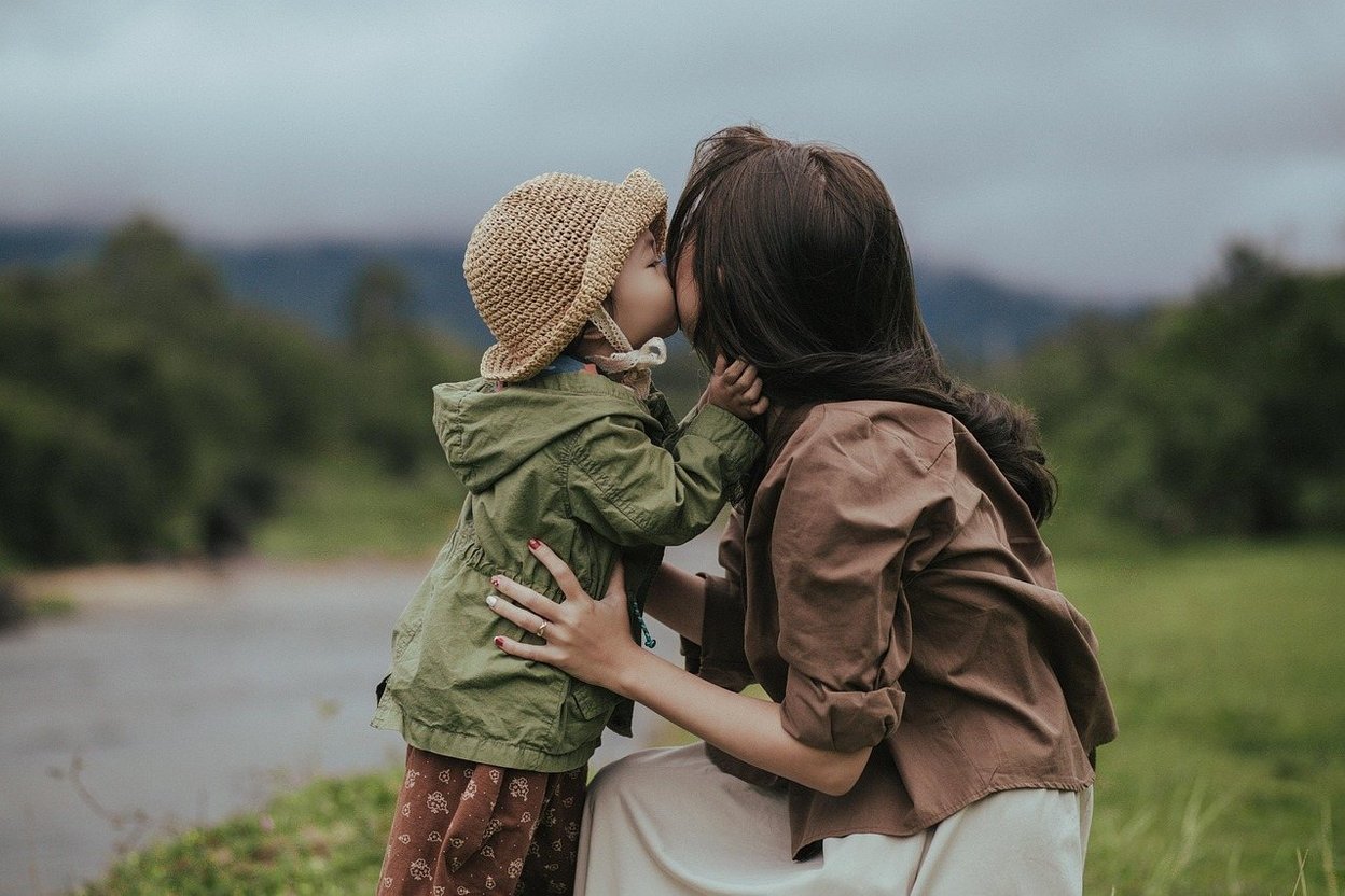A mother and child sharing a kiss outdoors in a grassy field.