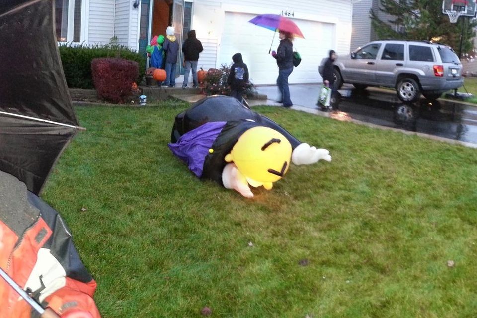 Trick-or-treaters with umbrellas going house to house on a rainy Halloween evening in a suburban neighborhood